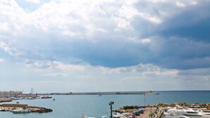 A marina with boats, a sandy beach, and a distant cityscape under a cloudy sky. - Bluemarine Apartment (Gallipoli)