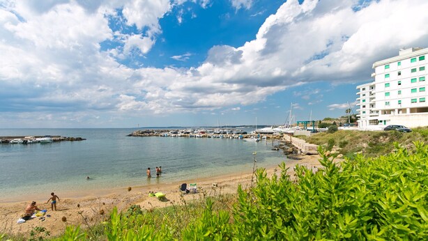 A coastal scene with a sandy beach, boats, and a building with balconies. - Bluemarine Apartment (Gallipoli)