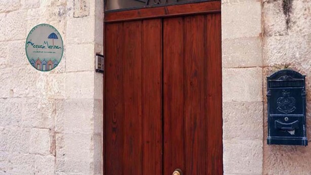 Eine Holztür mit Messingklinke, einem Briefkasten und einem runden Schild an der Wand.