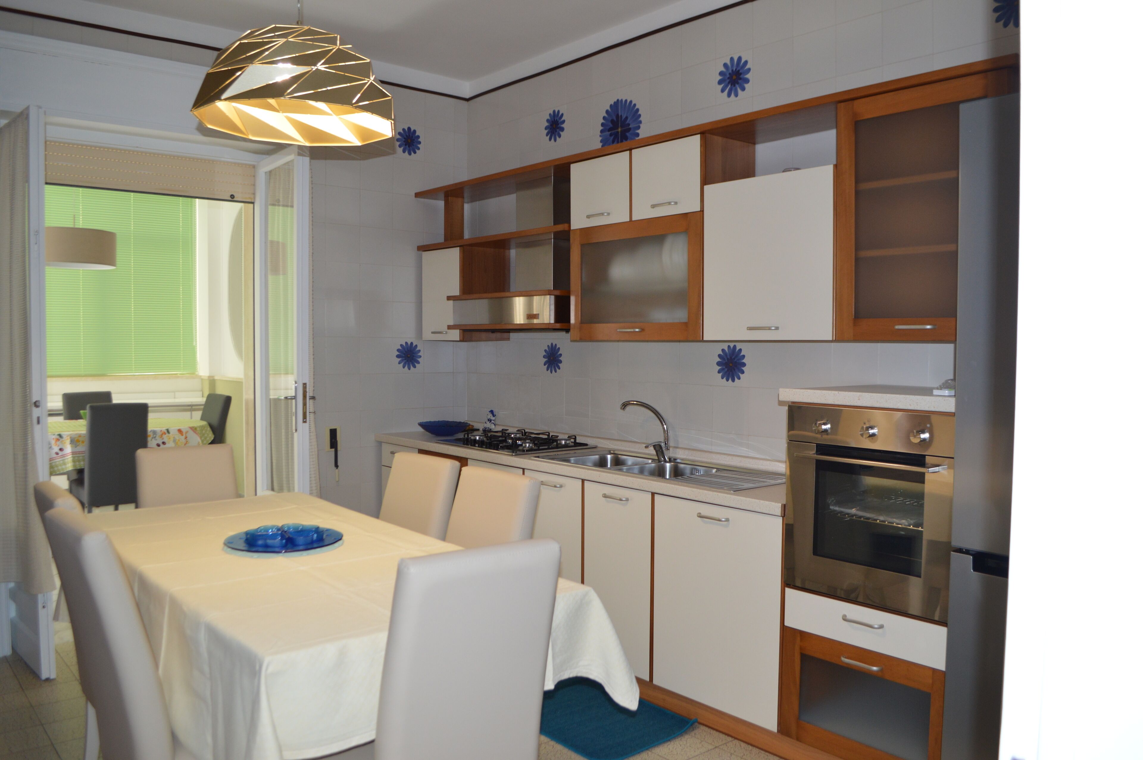A modern kitchen with white cabinets, a built-in oven, and a dining area with a table and chairs.