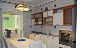 A modern kitchen with white cabinets, a built-in oven, and a dining area with a table and chairs. - Gallipoli Apartment - Activelife (Gallipoli)