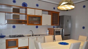 A modern kitchen with white cabinets, a gas stove, a sink, and a dining table with chairs. - Gallipoli Apartment - Activelife (Gallipoli)