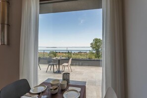 Un espace repas offrant une vue sur la mer et un balcon avec des sièges pour l’extérieur.