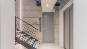 Un interior moderno con una escalera que conduce al primer piso, una puerta cerrada y una lámpara fijada a la pared.