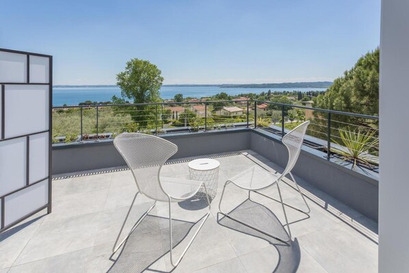 A balcony with two metal chairs and a small round table, overlooking a scenic view of a body of water and distant landscape. - Room-insula Felix - Deluxe Double Room w (Moniga del Garda)