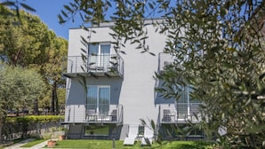 Un edifici modern de dos pisos amb balcons, una zona de jardí i cel blau.