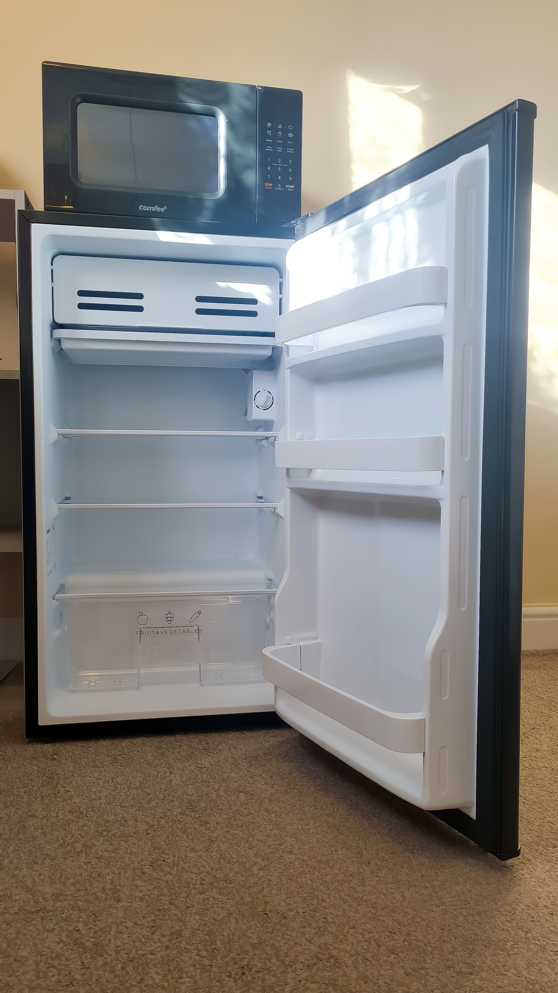 An open refrigerator with a microwave on top, clear interior shelves, and a 'Fruit & Vegetable' section.