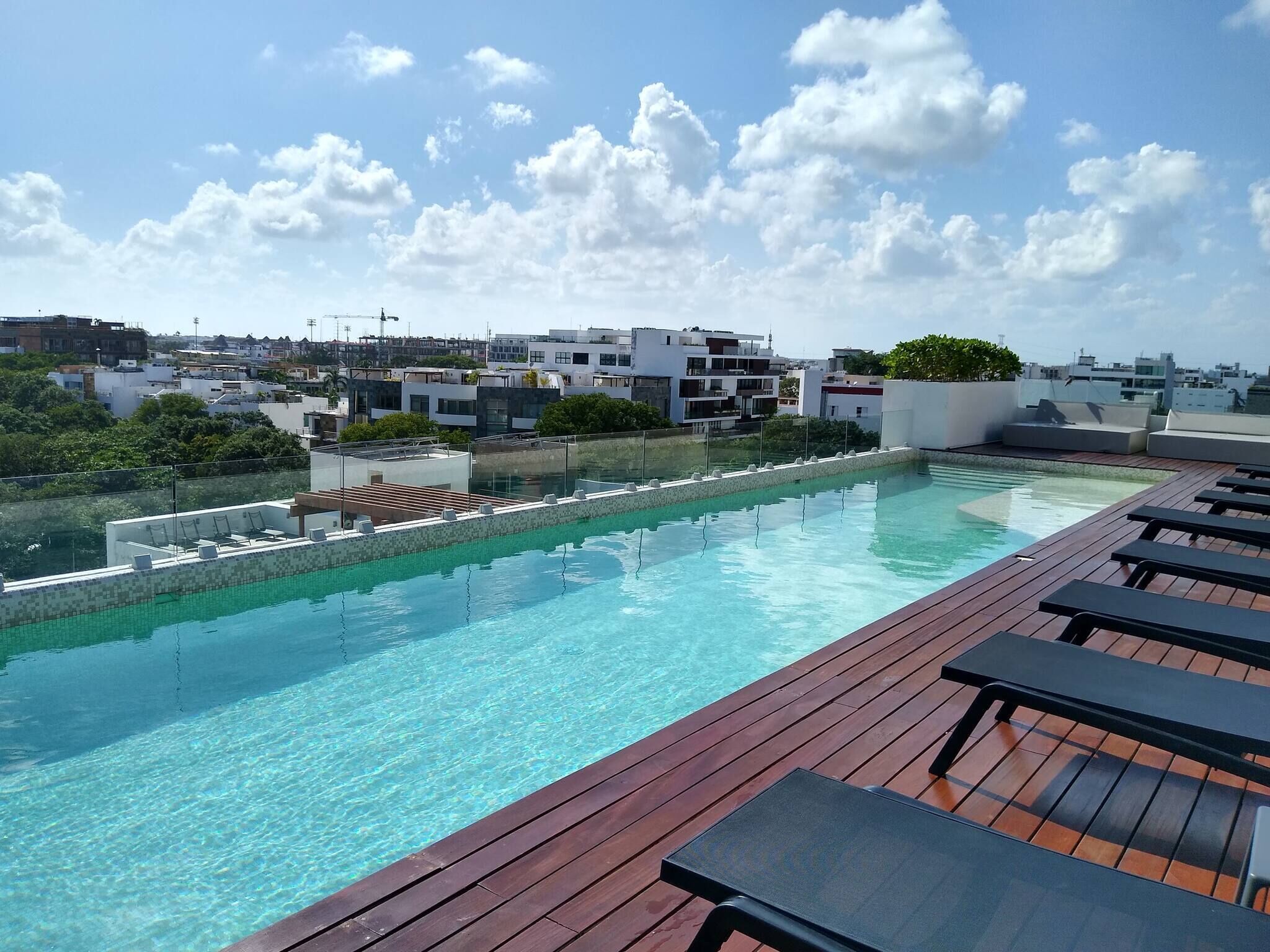 A rooftop pool with clear blue water, surrounded by wooden deck and lounge chairs.