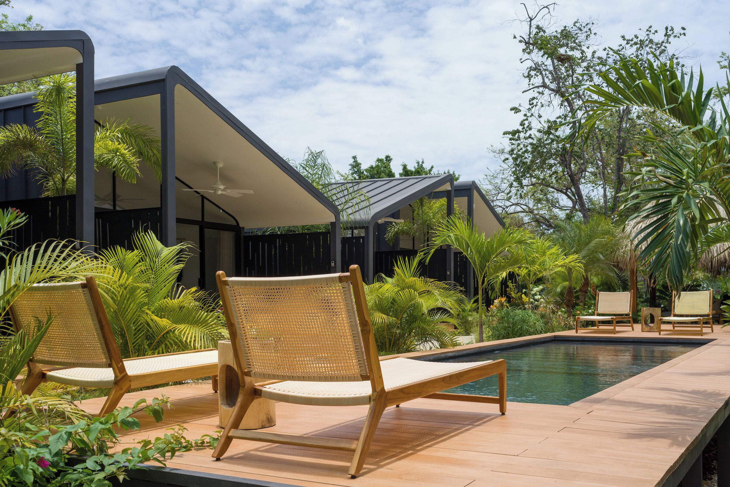 A poolside area with lounge chairs, a swimming pool, and lush greenery.