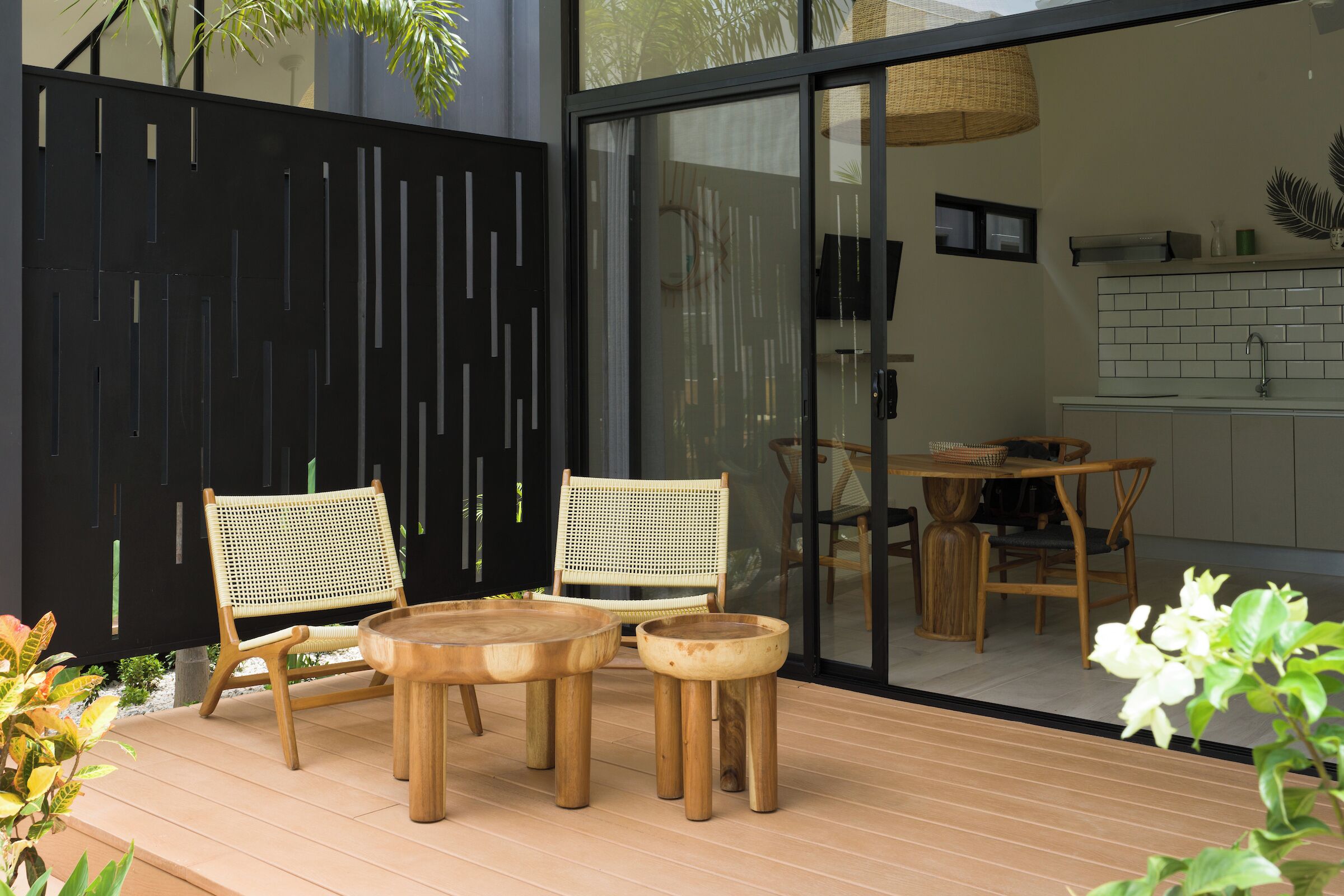 Une terrasse extérieure avec des meubles en bois, une clôture décorative noire et une vue sur l’intérieur d’un bâtiment moderne.