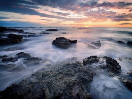 Una costa rocosa con olas, un atardecer y un cielo despejado.