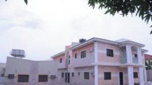 A multi-story building with a flat roof, a water tank on the roof, and a paved ground area. - Room-dilida Guest Suites - Guest Room (Abuja)