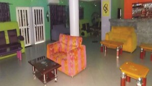 A lobby with a green wall, a purple sofa, a pink and orange sofa, and a yellow sofa. There are two small tables with metal legs. - Room-sheriffyt Royale Hotel - Guest Suit (Ikorodu)