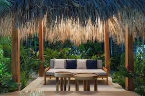 A thatched-roof outdoor seating area with a sofa and two round tables, surrounded by lush greenery. - 3 Favela Chic Tamarindo Adults Only Bungalow (Tamarindo)
