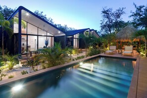 Une maison moderne dotée d’une piscine, d’un espace salon extérieur et de plantes tropicales.
