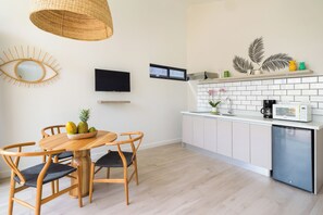 Une cuisine moderne avec des meubles blancs, un lave-vaisselle en acier inoxydable, une table à manger en bois avec des chaises, un luminaire suspendu en fibres tressées et des œuvres d’art décoratives sur les murs.