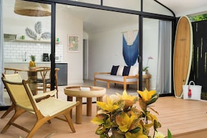 A modern living space with a glass door leading to a kitchen, a wooden dining table, and a surfboard. - 5 Favela Chic Adults Only 2 Bedroom Bungalow (Tamarindo)