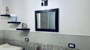 A bathroom with a white sink, a mirror with a black frame, and decorative shelves with items like a vase and a jar of seashells. - All the Comforts of a Hotel With the Spaces of a Home (Castellammare di Stabia)