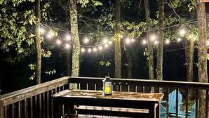 Een houten terras met een tafel, bankjes, lichtslingers en een lantaarn.