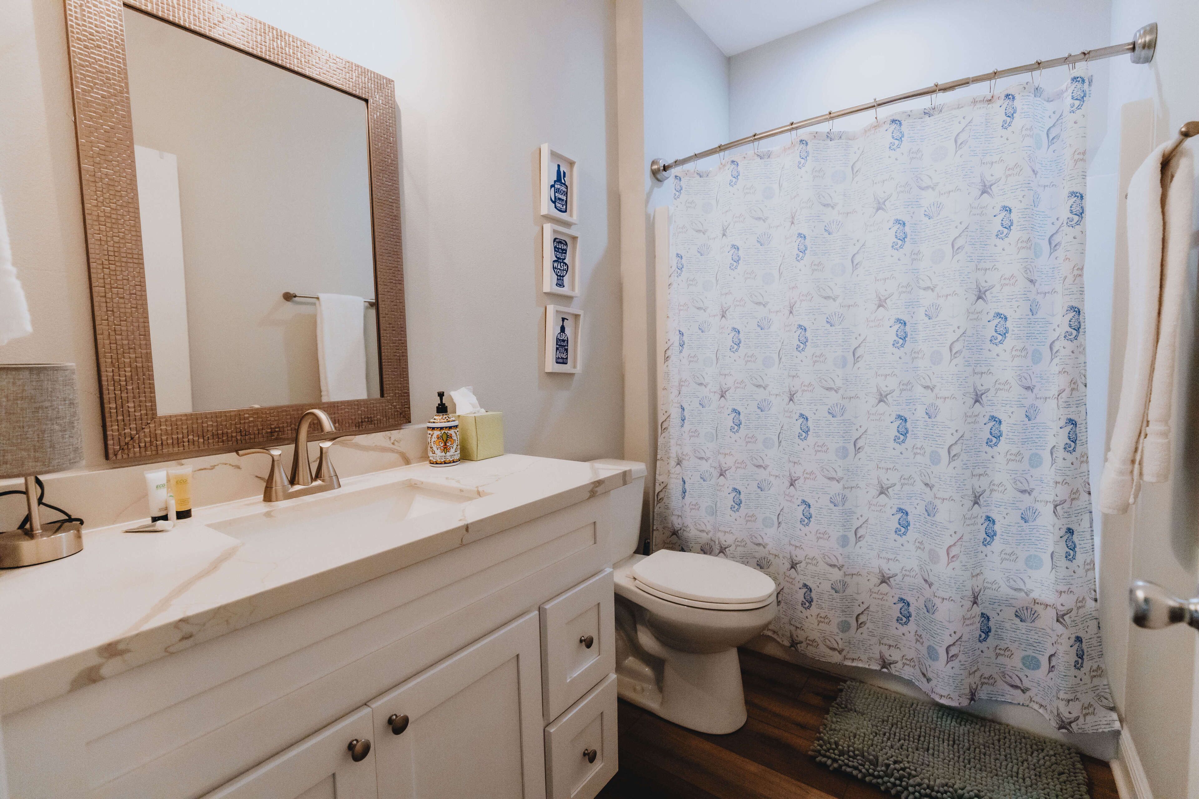 A bathroom with a white sink, a large mirror, a toilet, and a shower curtain with a nautical pattern.