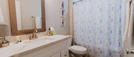 A bathroom with a white sink, a large mirror, a toilet, and a shower curtain with a nautical pattern.