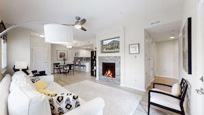 A modern living room with a fireplace, a dining area, and a kitchen in the background. - Lavish Tranquil No-Steps Oasis (Westminster)