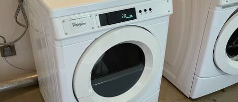 Dos lavadoras Whirlpool de carga frontal blancas en un lavadero con piso de concreto y un enchufe eléctrico instalado en la pared.