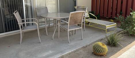 Un patio con una mesa y sillas, una puerta corrediza de vidrio y una valla de madera.