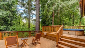 A wooden deck with two wicker chairs and a small table, surrounded by tall trees. - Spacious Cabin with Hot Tub, Sauna, AC, Loft, King bed, Free Parking (Seattle)