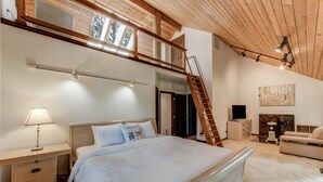 A bedroom with a large bed, a desk with a lamp, a dresser, a ladder to a loft, and a painting on the wall. - Spacious Cabin with Hot Tub, Sauna, AC, Loft, King bed, Free Parking (Seattle)