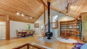 A spacious living area with a wooden ceiling, a large fireplace, a dining table with chairs, and a leather sofa. - Spacious Cabin with Hot Tub, Sauna, AC, Loft, King bed, Free Parking (Seattle)