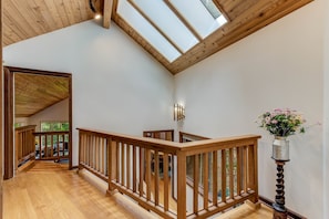 A wooden staircase with a railing, leading to a room with a skylight and a vase with flowers. - Spacious Cabin with Hot Tub, Sauna, AC, Loft, King bed, Free Parking (Seattle)