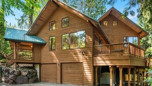 A two-story wooden cabin with a balcony, a garage, and a stone foundation. - Spacious Cabin with Hot Tub, Sauna, AC, Loft, King bed, Free Parking (Seattle)