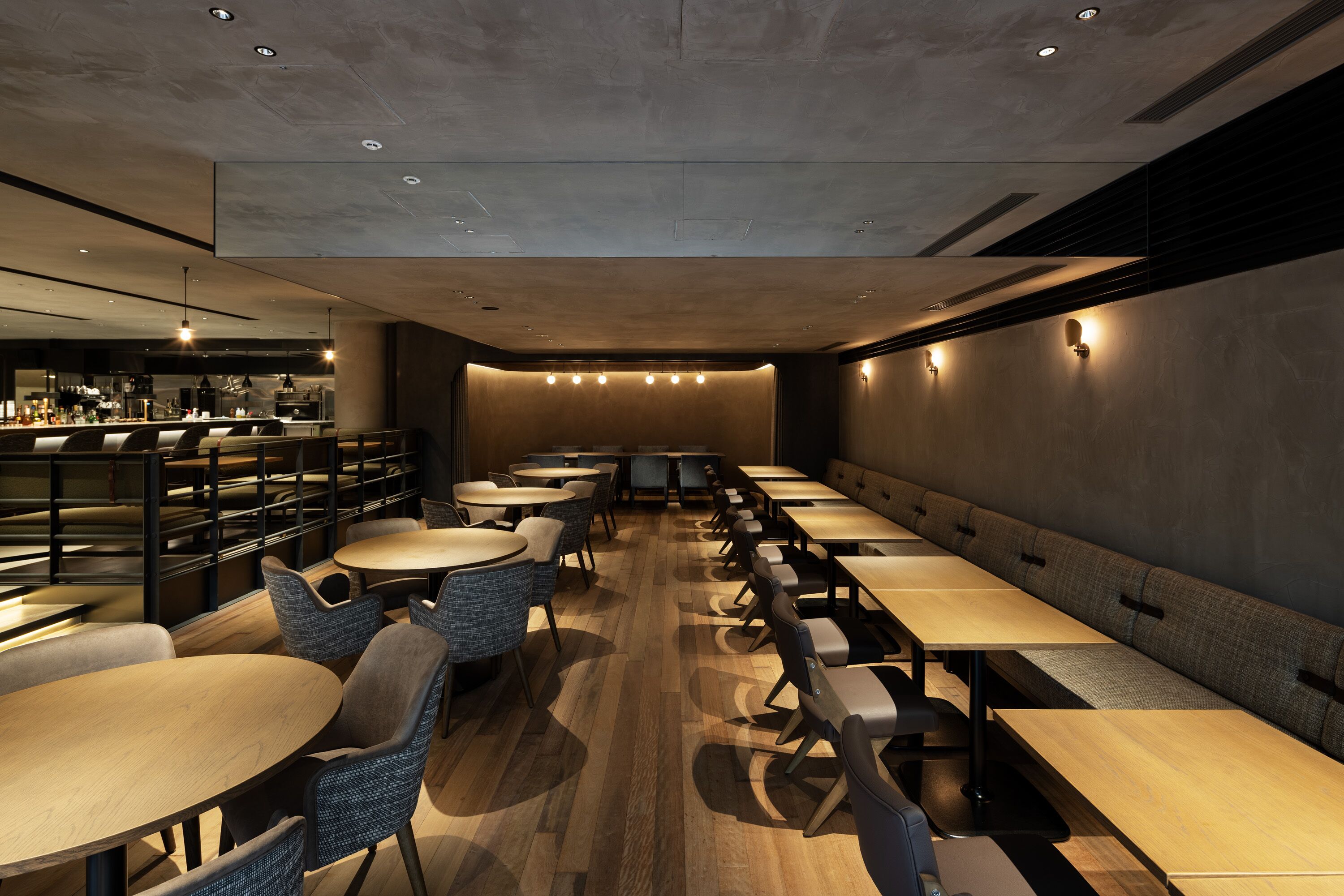 A modern restaurant with long communal tables and booths, a bar area in the background, and a wooden floor.