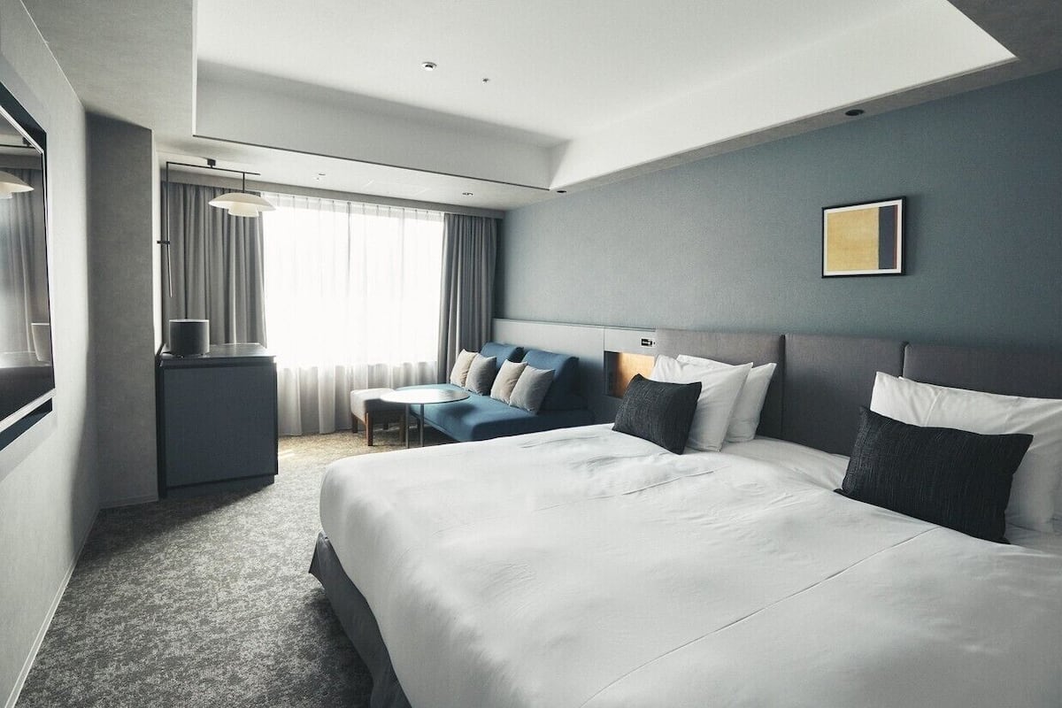 Une chambre d’hôtel moderne équipée de deux grands lits, d’un bureau, d’une chaise et d’une grande fenêtre avec des rideaux.