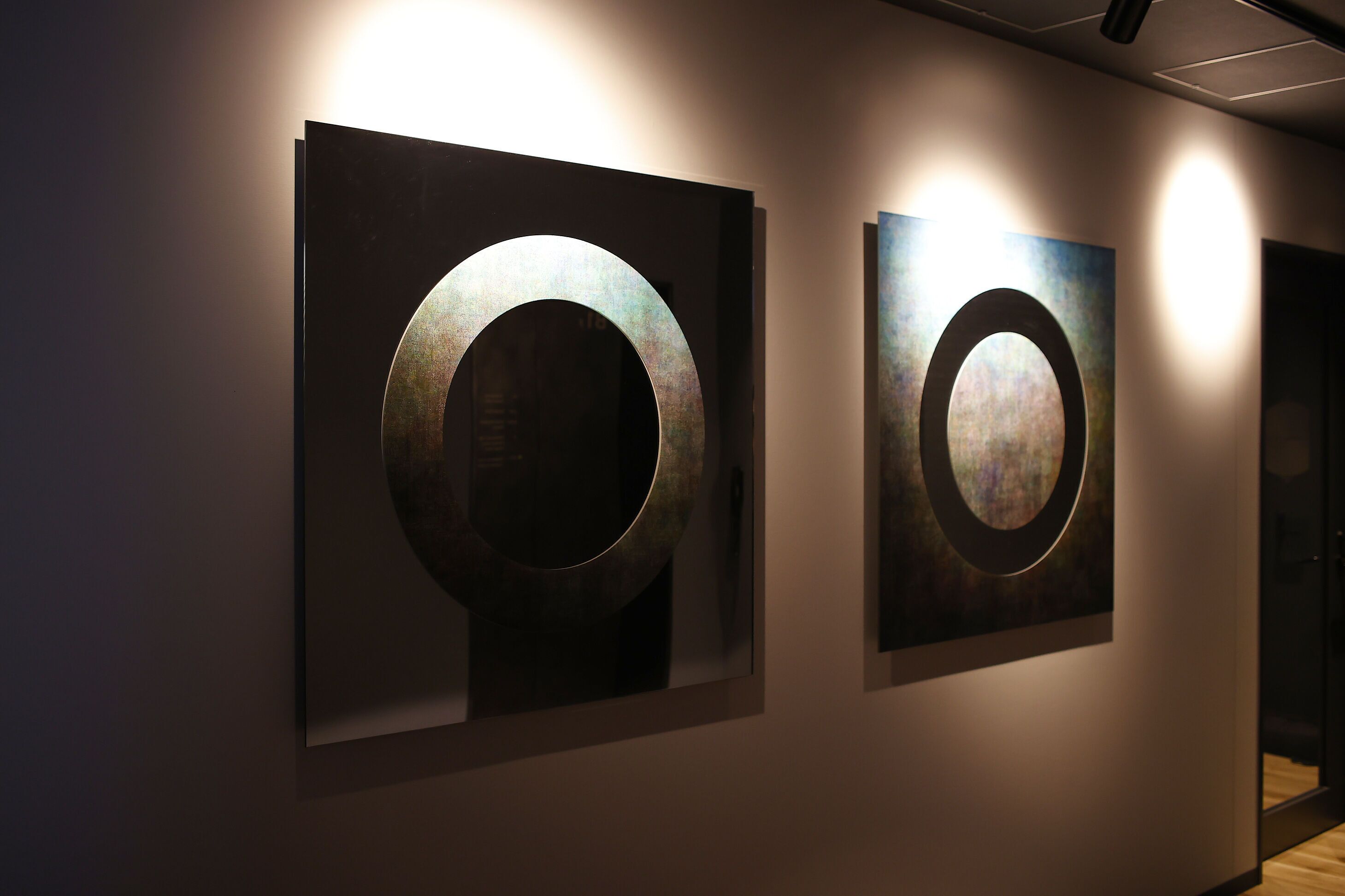 Two framed circular artworks on a wall in a hallway.