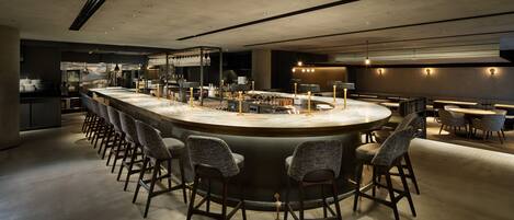 A modern bar area with a curved counter, bar stools, and ambient lighting.