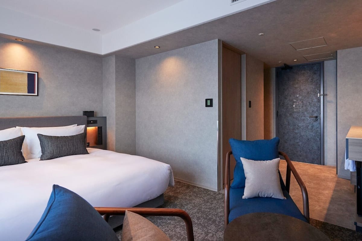 Une chambre d’hôtel moderne dotée d’un grand lit, d’un coin salon avec des fauteuils, d’une cheminée et d’une petite kitchenette.