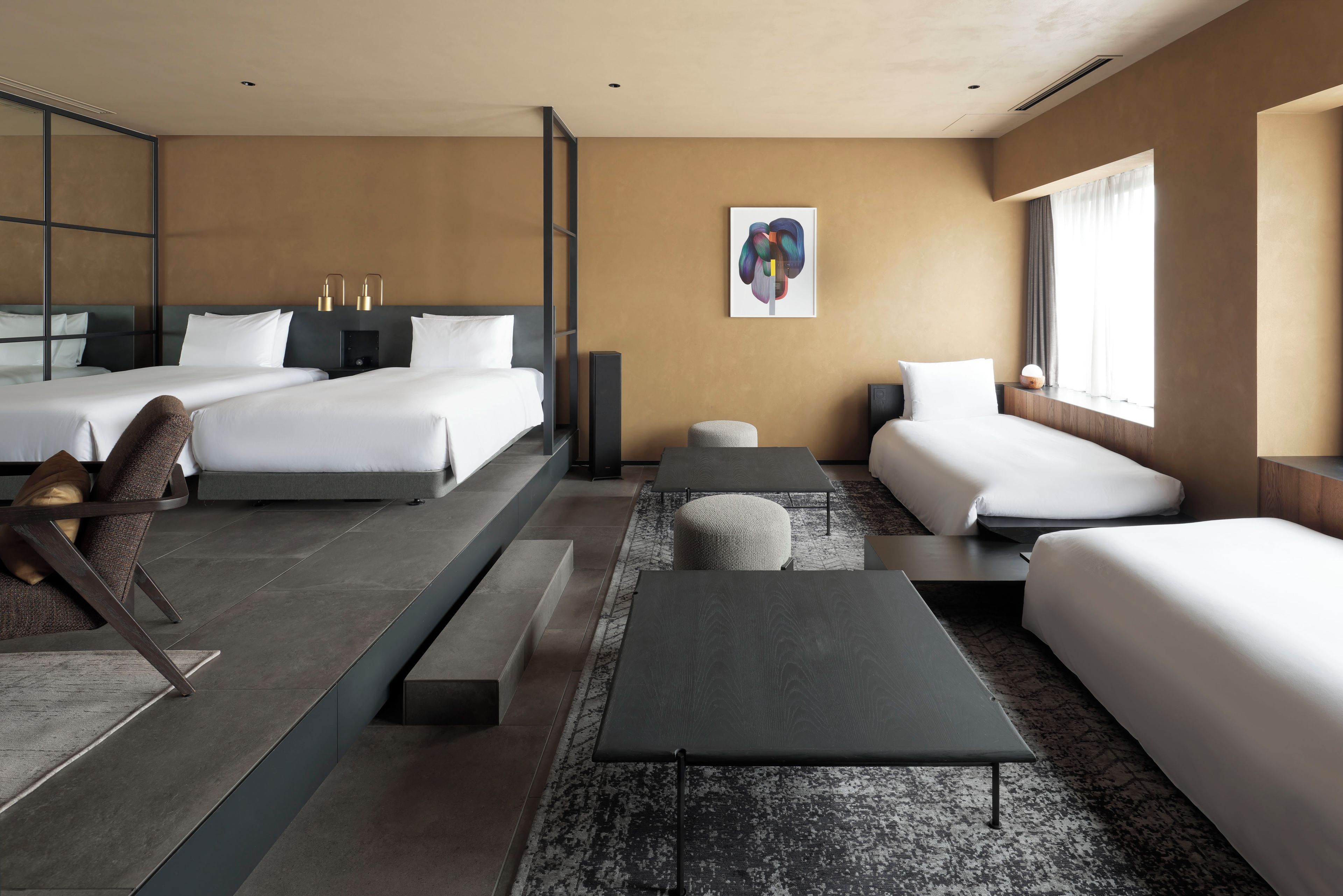 A modern hotel room with two beds, a sofa, a small table, and a large window.