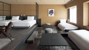 A modern hotel room with two beds, a sofa, a small table, and a large window.
