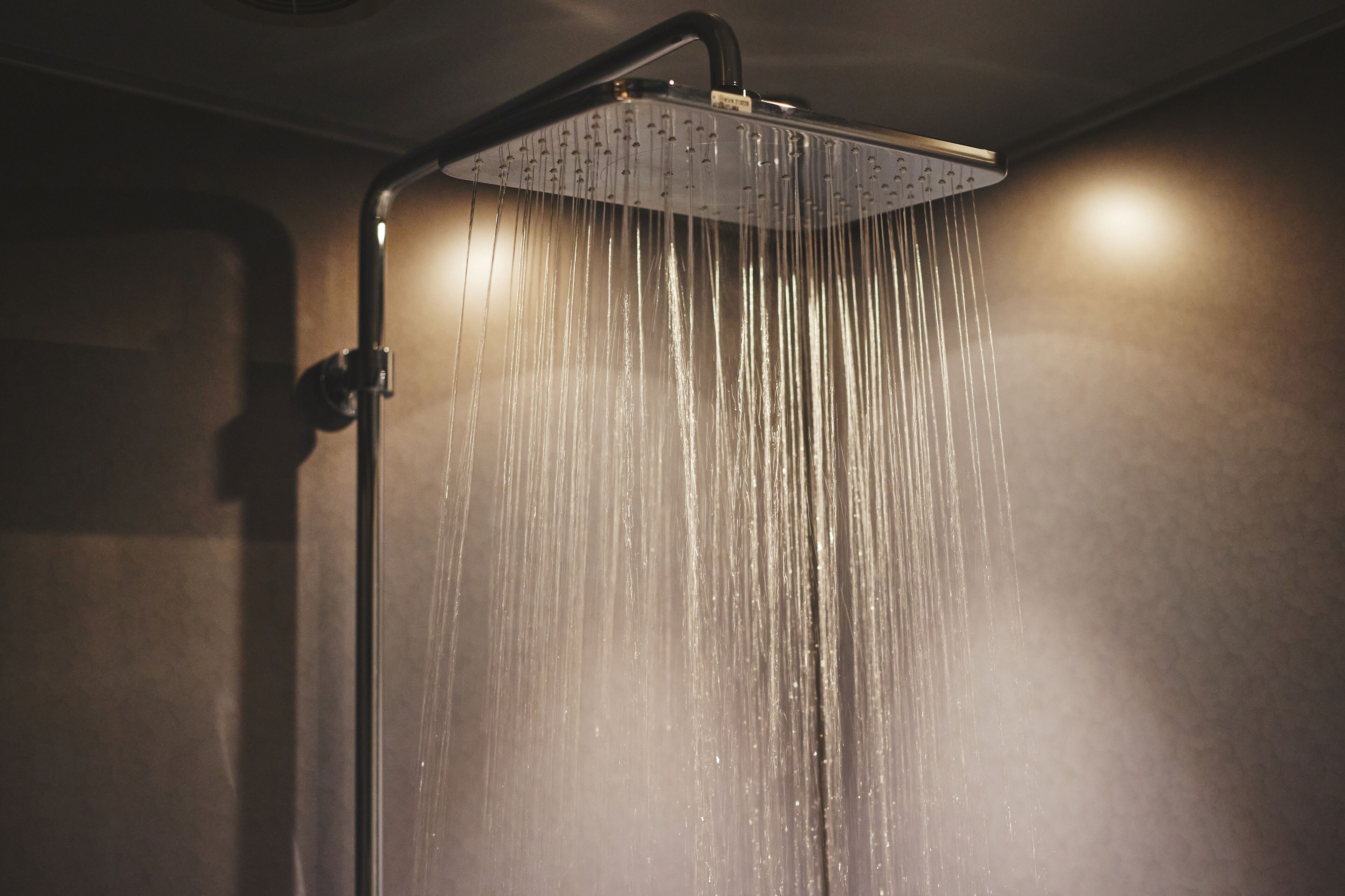 A showerhead with multiple nozzles, water flowing from it, and a wall-mounted control panel.