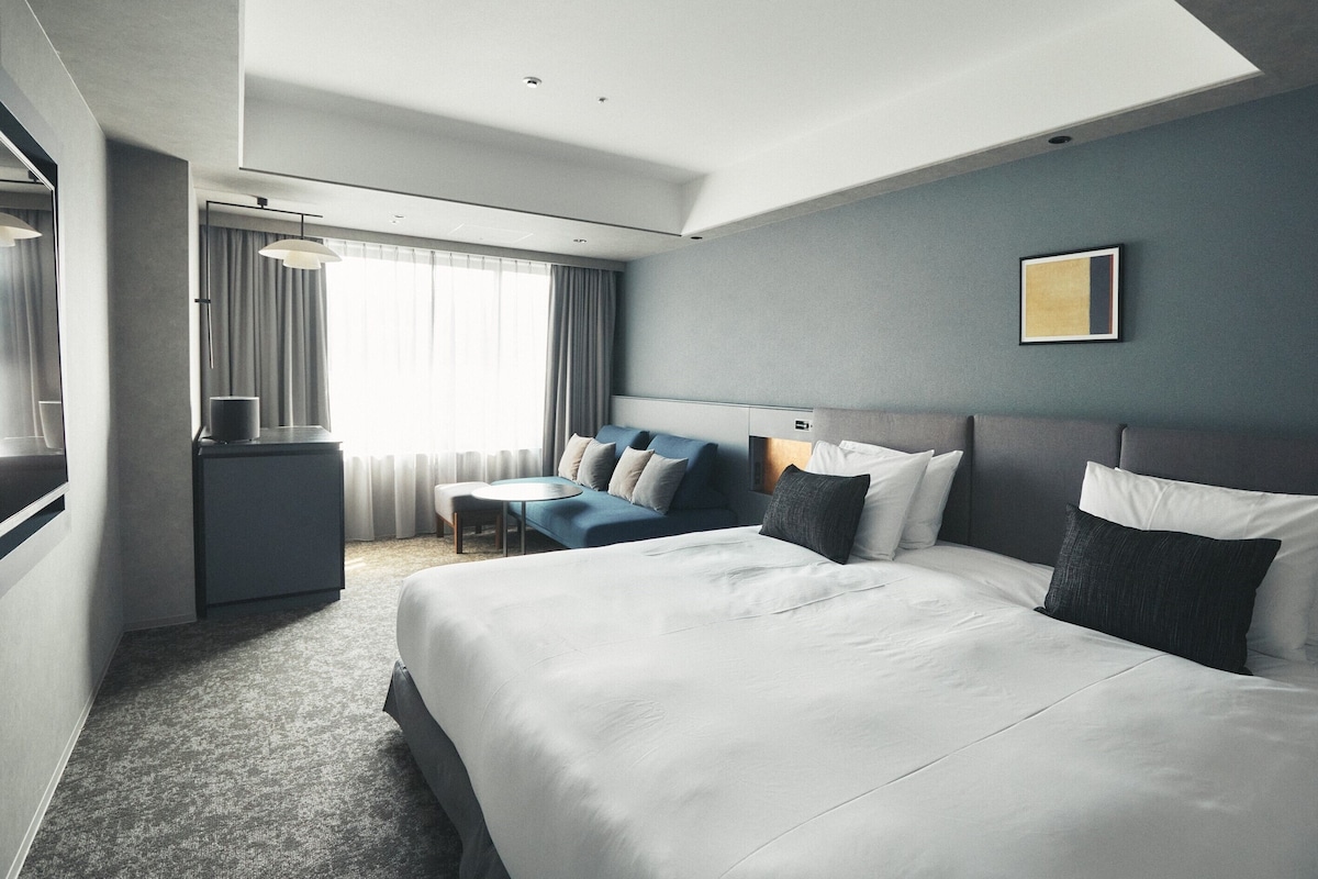 A hotel room with a large bed, a sofa, a desk, and a window with curtains.