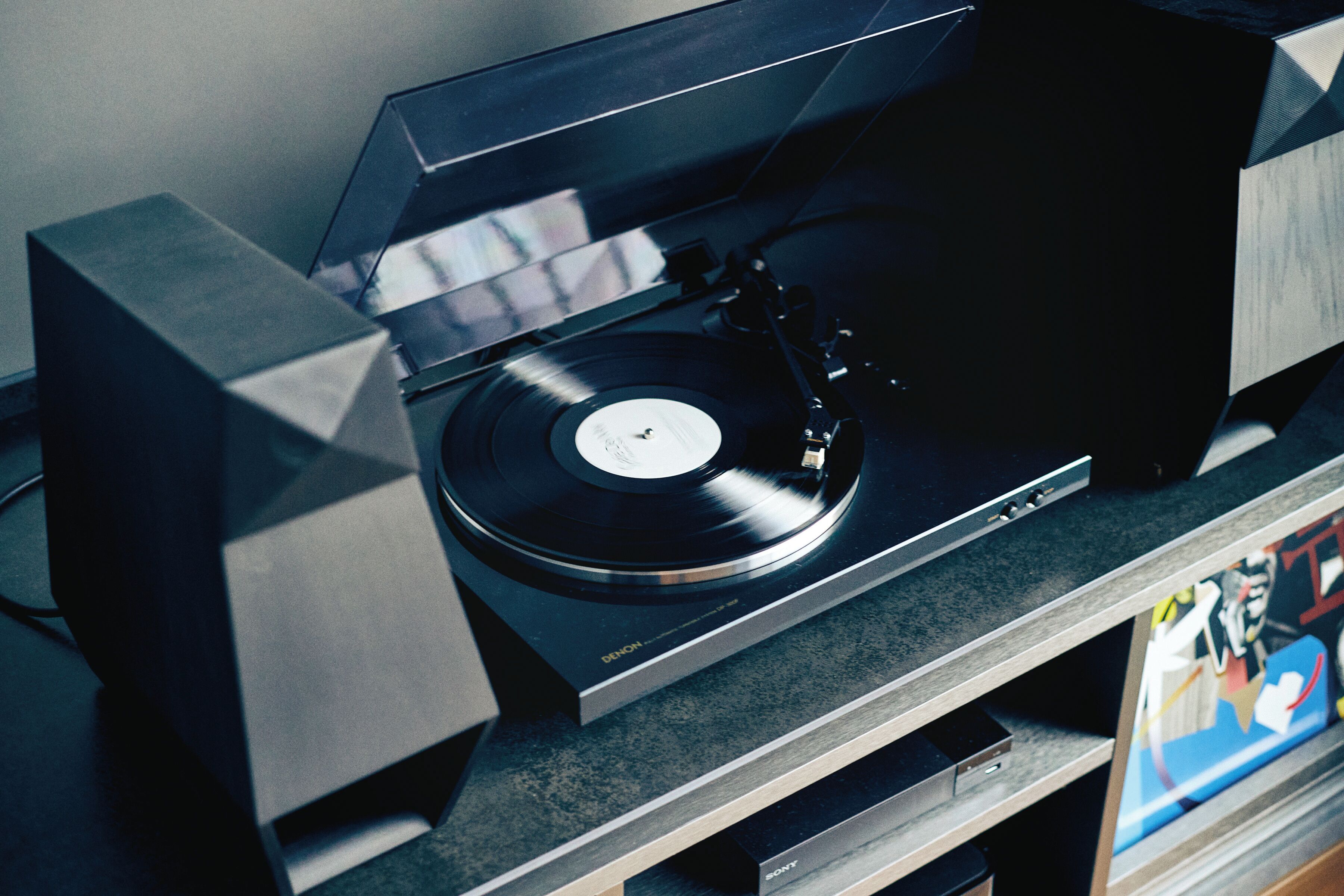 Une platine vinyle avec un disque, une enceinte et une étagère sur laquelle se trouve un livre.