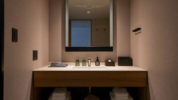 A modern bathroom with a wooden vanity, a large mirror, and a sink. There are towels and toiletries on the vanity.
