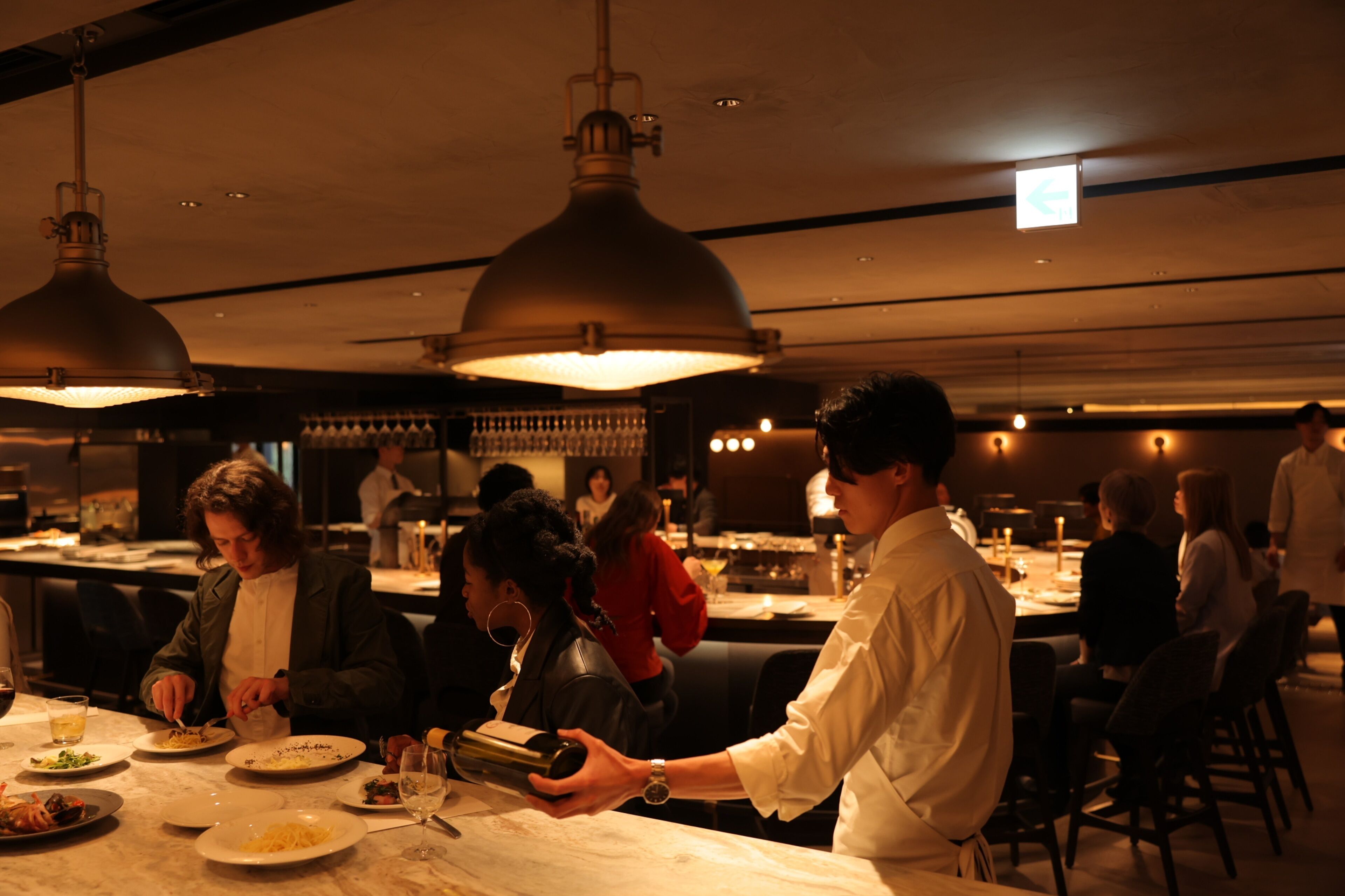 Ein Restaurant mit gedeckten Tischen, Deckenbeleuchtung und einer Bar im Hintergrund.