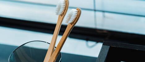 Two wooden toothbrushes in a clear glass cup on a black surface.