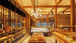 Una panadería con vigas de madera, una mesa central de exhibición y estantes llenos de productos horneados.