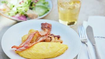 A plate with an omelet, bacon, and beans, a glass of iced tea, and a side salad on a table.
