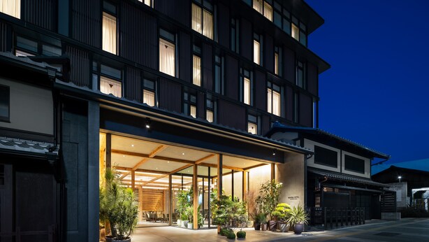 Un hotel moderno con fachada tradicional, amplia entrada de cristal y plantas en macetas afuera.