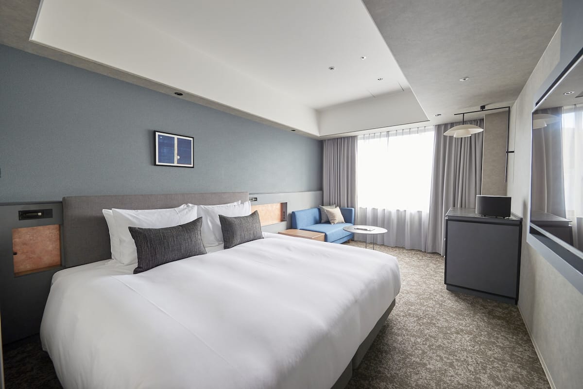 Une chambre d’hôtel avec un grand lit, un petit bureau, un canapé et une fenêtre avec des rideaux.